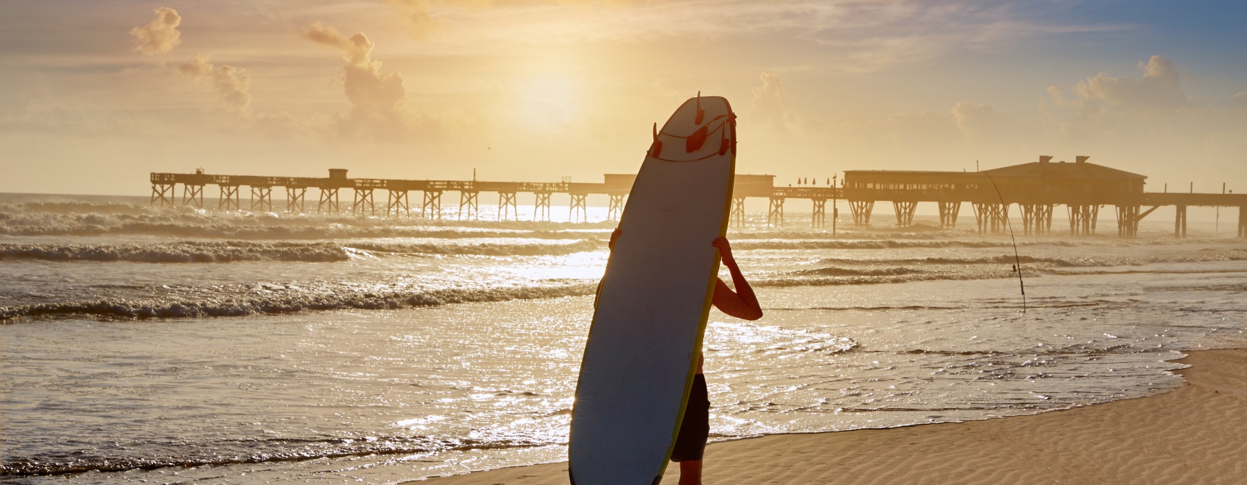 surfer carrying surfboard on back walking along beach shoreline ocean water daytona beach pier